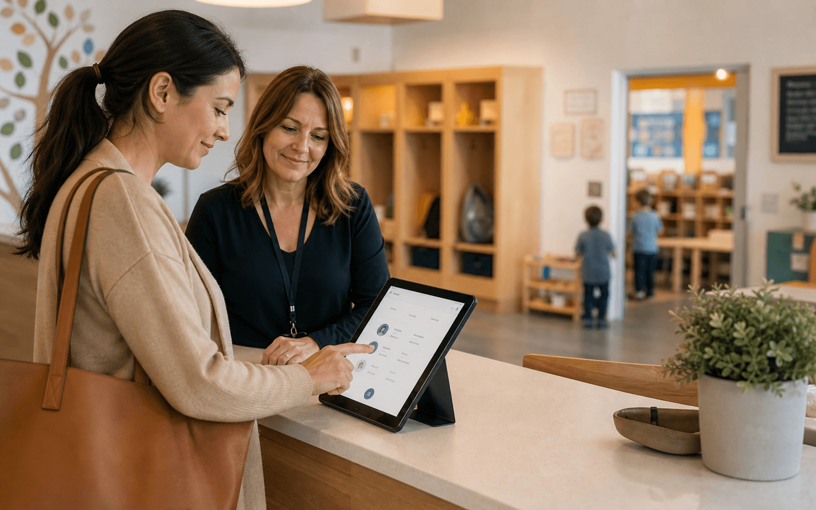 Parent using a tablet kiosk with a school director in a childcare lobby